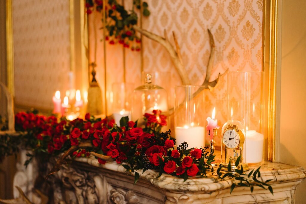 Vintage clock, floral compositions and candles on decorated fireplace. Event design.
