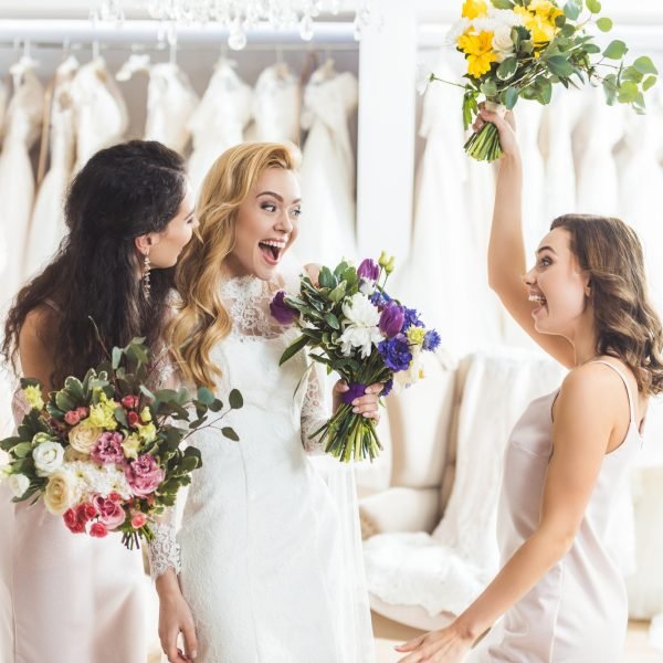 Smiling women in wedding dresses with flowers in wedding atelier Smiling women in wedding dresses with flowers in wedding atelier